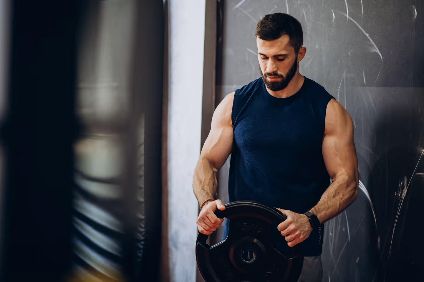 Muscular man in a sleeveless shirt holding a weight plate in a gym.