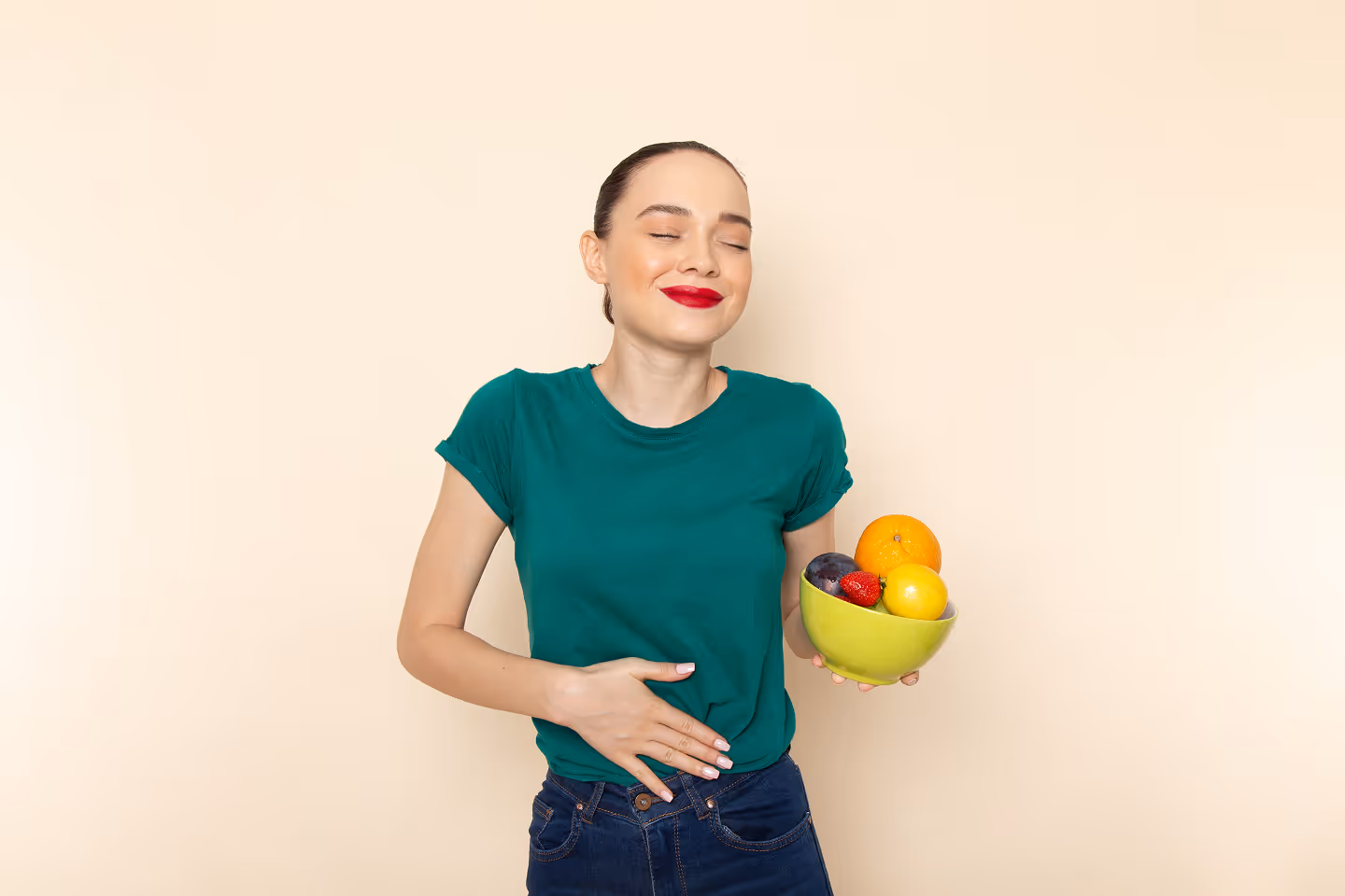 Front view of a young, attractive woman holding a bowl of fresh fruits. She’s happy with her stomach being bloat-free and pain-free.